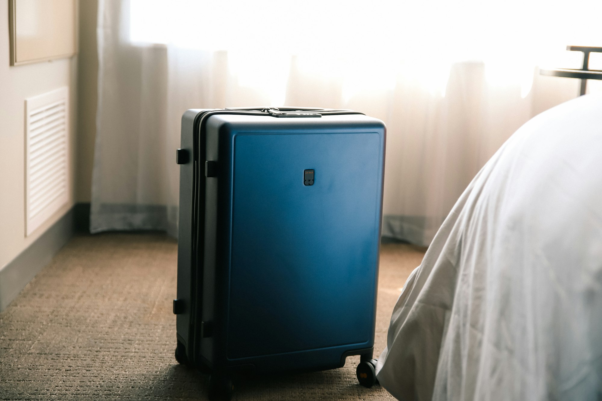 Valise minimaliste bleue à roulettes posée dans une chambre d'hôtel épurée